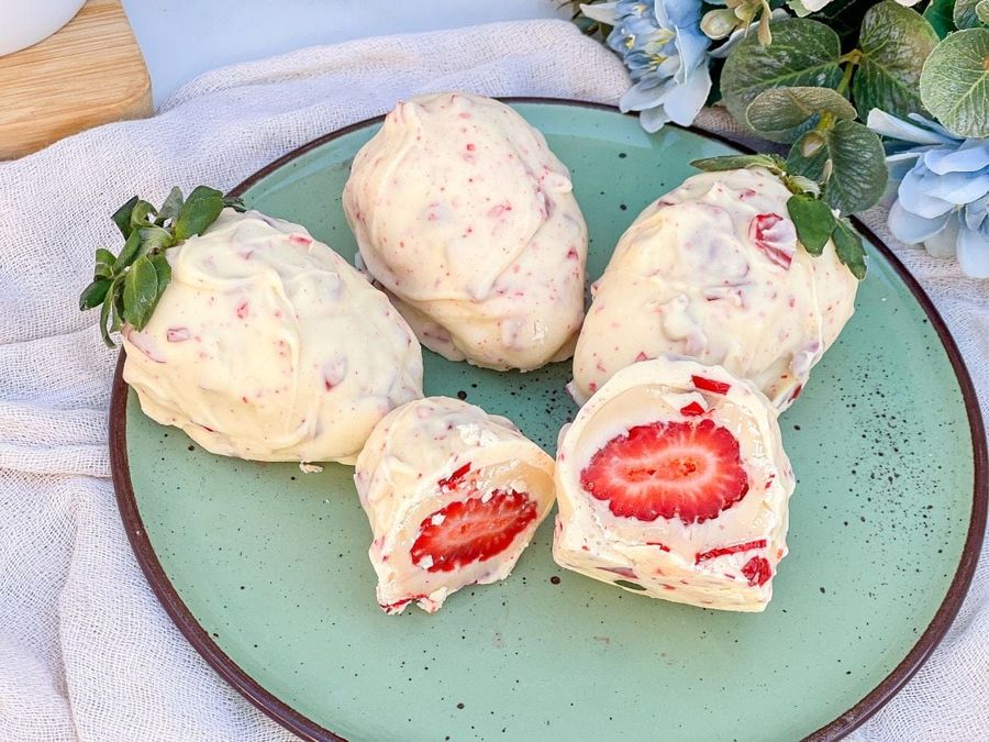 Morangos cobertos com chocolate branco e pedaços de morango, um cortado ao meio